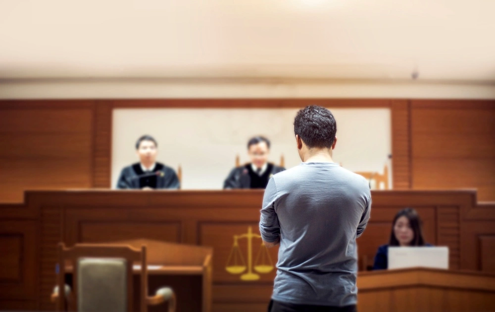 A man in a courtroom, standing in front of a judge, being convicted of a DUI offense
